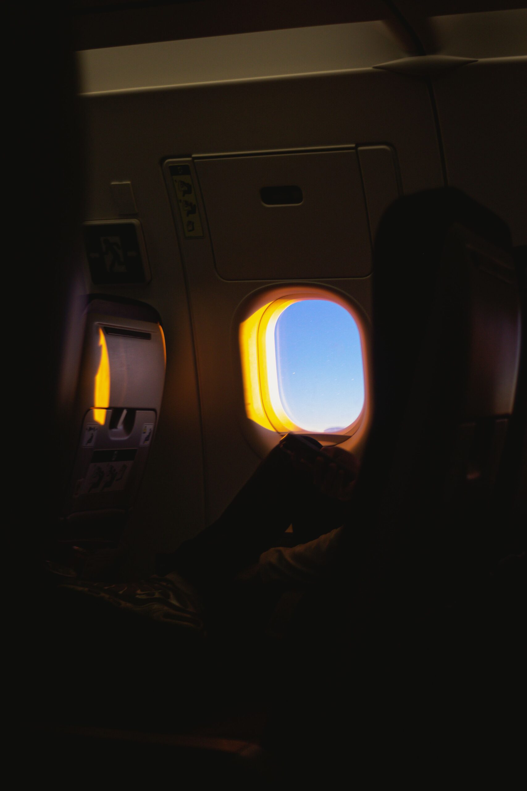 Silhouette of a passenger resting by an airplane window at sunrise