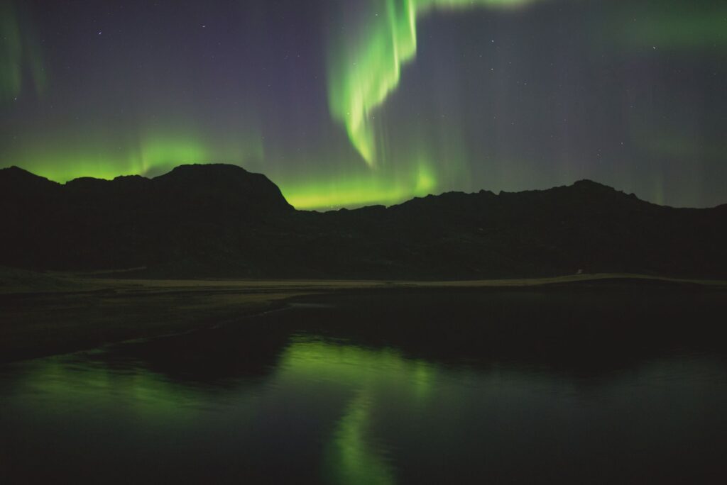 Green northern lights over a still lake and mountains in Iceland at night